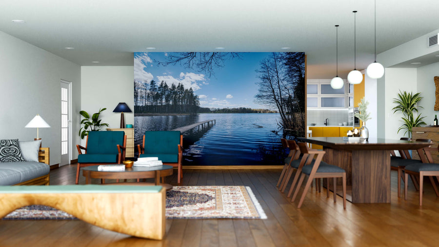 A bright, modern open-plan living and dining area with wood furniture and blue chairs features the Lakeside Escape Wall Mural, depicting a serene lake with trees and a dock for a tranquil, nature-inspired focal point.