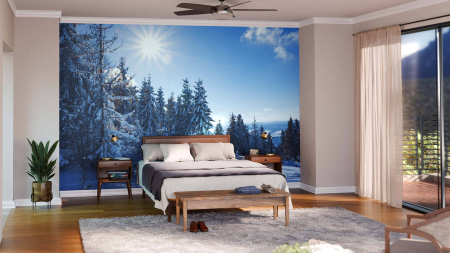 A cozy bedroom features a bed, nightstands, modern decor, and a “Landscape Of A Winter Forest Wall Mural” behind the bed. Sliding glass doors bring in natural light and reveal a balcony outside.