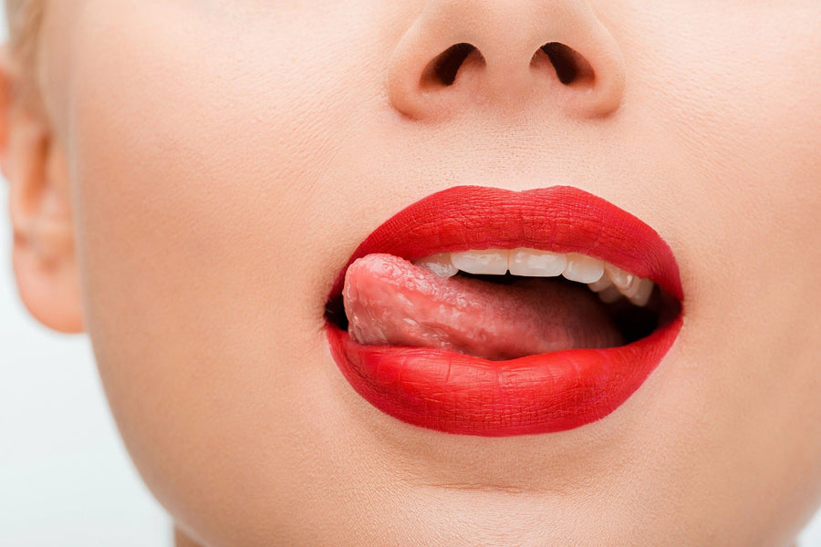 A close-up of a woman's lower face with red lipstick licking her upper lip playfully, evoking sensuality—just like the Lip Tease Wall Mural makes a bold statement in your space.