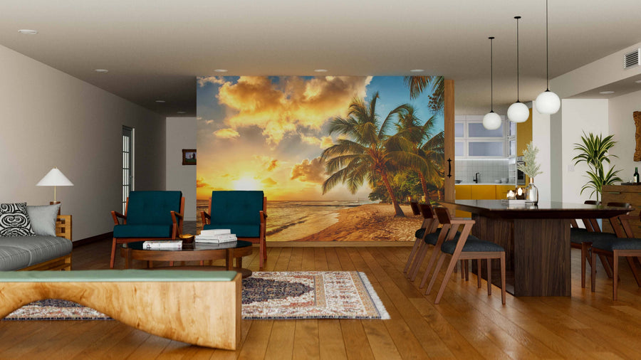 A modern open-concept living and dining room with wooden floors, teal chairs, and pendant lights is highlighted by the vibrant Barbados Wall Mural, depicting a tropical beach sunset with palm trees as a relaxing focal point.