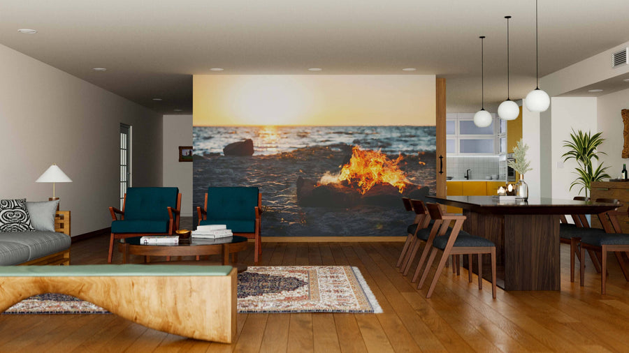 A modern living-dining room with wood floors and mid-century furniture features a large Beach Bonfire Wall Mural on the back wall, adding warmth and depth to the cozy space. Pendant lights hang above the neatly arranged dining table.