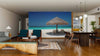A modern living-dining room with wooden floors and mid-century furniture features the Beach Chairs and Umbrella Wall Mural, showcasing a beach scene that brings a relaxing, tropical vibe to the space.