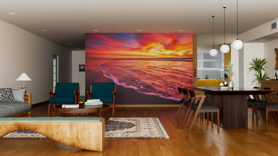 A modern open-plan living and dining area with wood floors, teal armchairs, and a dining table is enhanced by the Beautiful Sunset in the Ocean Wall Mural, creating a vibrant focal point amid contemporary decor.