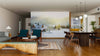 Modern living and dining room with wooden floors, stylish furniture, and a Big Winter House Mountain Wall Mural depicting a snowy village at sunrise. Blue and wooden chairs, a patterned rug, and a dark dining table under round pendant lights complete the space.