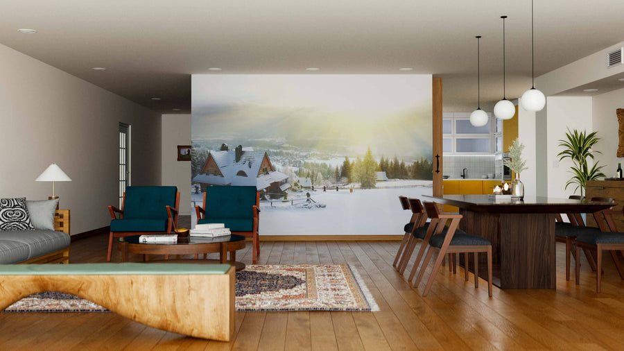 Modern living and dining room with wooden floors, stylish furniture, and a Big Winter House Mountain Wall Mural depicting a snowy village at sunrise. Blue and wooden chairs, a patterned rug, and a dark dining table under round pendant lights complete the space.