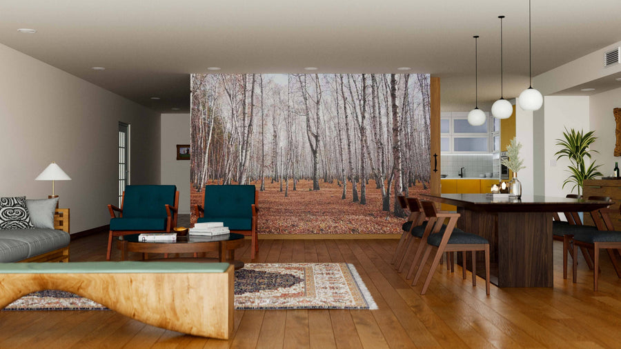 A modern living-dining room features wooden floors, teal chairs, a patterned rug, and the Birch Trees After Autumn Wall Mural. The dining area includes a dark table, six chairs, globe pendant lights, and an open view of the kitchen.