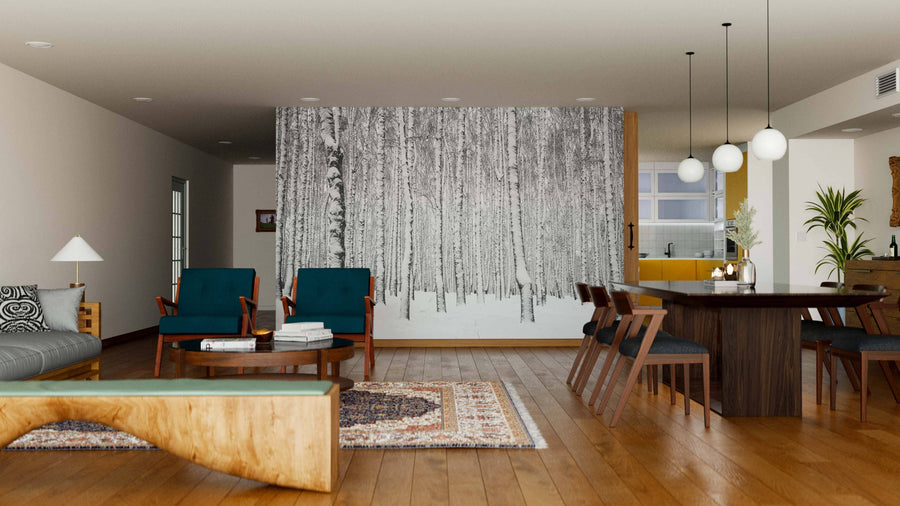 A spacious, modern living and dining area has wood floors, teal chairs, a unique wooden coffee table, and a large Black and White Birch Trees Wall Mural. The dining table seats eight with pendant lights above and an open kitchen in the background.