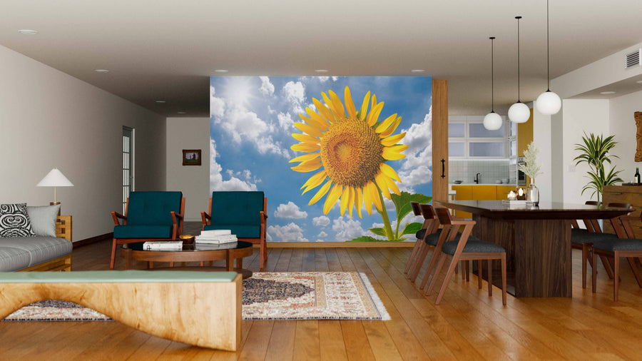 A modern living-dining room with wooden floors and mid-century furniture features the Blue Sky and Sunflower Wall Mural, a peel-and-stick design displaying a large sunflower against blue sky, adding vibrant color. The kitchen is visible in the background.