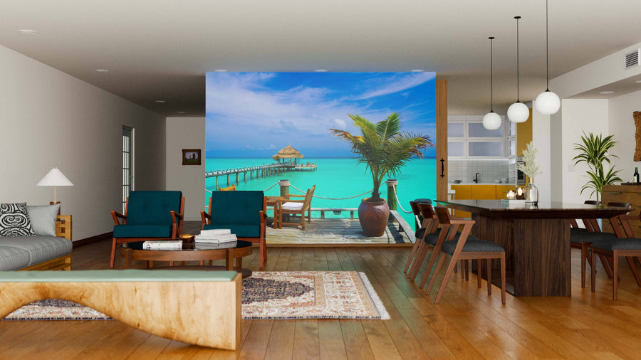 A modern living-dining room with wooden floors and mid-century furniture is enhanced by the Cafe by the Beach Wall Mural, bringing a striking, personalized beachy vibe with its vibrant depiction of a tropical pier over turquoise water.