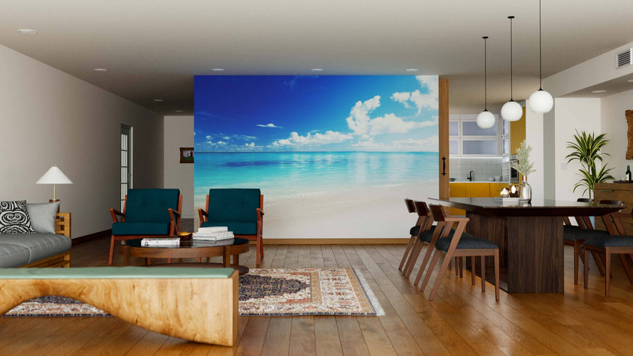 A modern living-dining room with wooden floors, teal chairs, and a wood dining table is enhanced by the Caribbean Sea Wall Mural—a large peel and stick mural depicting a serene beach scene for a relaxing, coastal vibe.