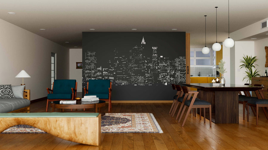 A modern living-dining room features wood floors, mid-century furniture, and the City Lights Wall Mural—a city skyline in white on a black accent wall. Pendant lights hang over the dining table with teal chairs and a blend of neutral and dark tones.