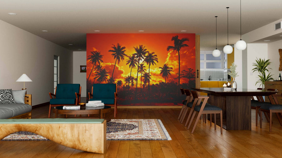 A modern open living-dining space features wood floors, teal chairs, a long dining table, pendant lights, and a Coconut Palms Wall Mural depicting palm trees at sunset, with a cozy kitchen in the background.