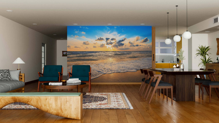 A modern living-dining area with wooden floors, teal chairs, a dark dining table, pendant lights, and the Colourful Sea Sunset Wall Mural featuring waves and golden sunlight creates an open, airy atmosphere.