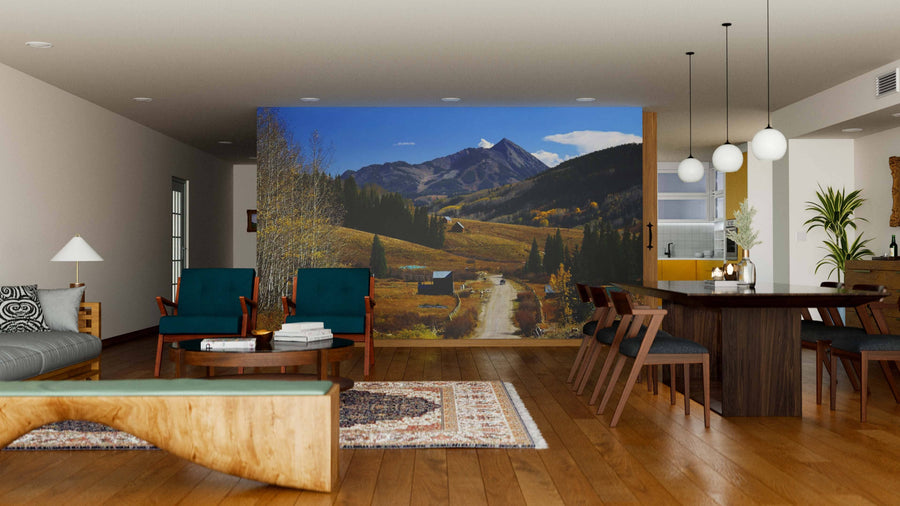 A modern living-dining room with wooden floors, green armchairs, and a dining table features the Crested Butte Mountain Wall Mural, creating an open, nature-inspired atmosphere perfect for relaxing or entertaining.
