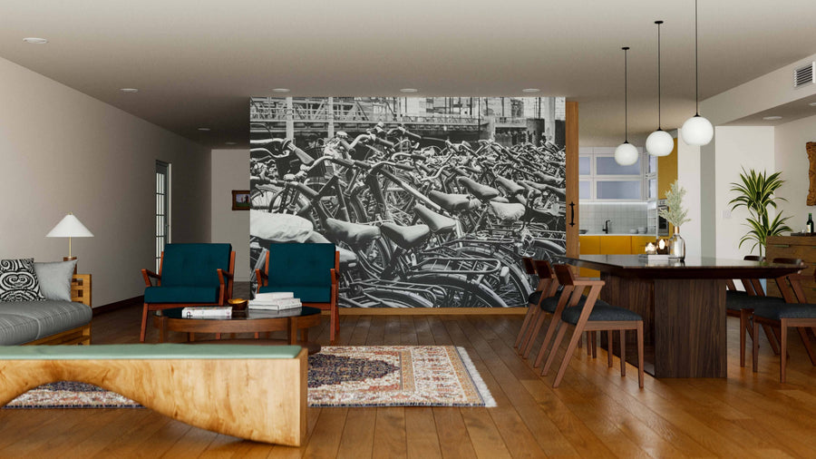 A modern living-dining room with wood floors, blue chairs, a wooden dining table, pendant lights, and the Cruisers Wall Mural featuring a black-and-white photo of tightly packed bicycles. Cozy minimal decor enhances the open space.