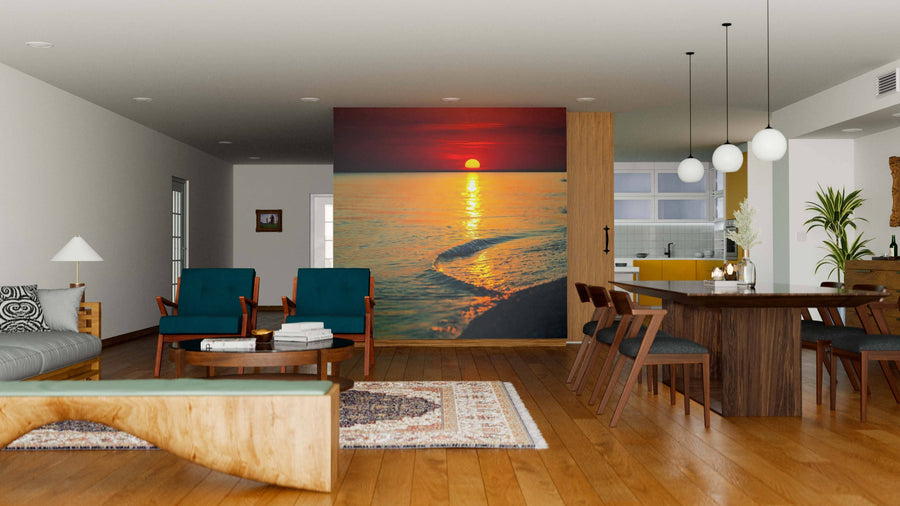A modern open living-dining area with wooden floors, teal armchairs, and pendant lights features the Dark Sea Sunset Wall Mural—a peel and stick mural showcasing an ocean sunset in orange and red tones as a vibrant focal point behind the seating area.