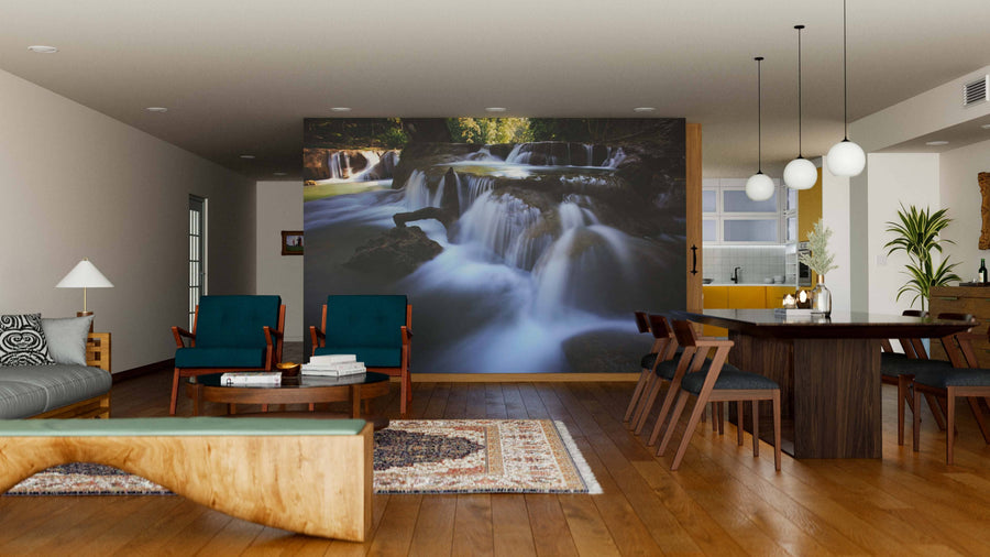 A modern living-dining room with wooden floors, teal chairs, a large dining table, and the Deep Forest of Thailand Wall Mural featuring a serene waterfall. The space is brightened by round pendant lights and accented with rugs and contemporary furniture.