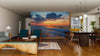 A modern open-plan living and dining room with wooden floors and mid-century furniture features the Empty Beach Wall Mural as a striking focal point, while warm lighting enhances the inviting atmosphere.