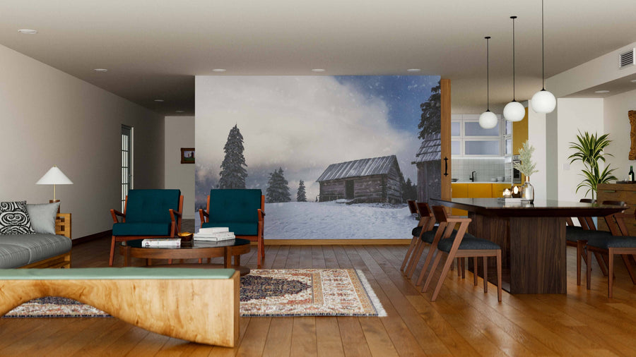 A modern open-concept living and dining area with wood floors and furniture features the Empty House on the Mountain Wall Mural. Blue armchairs, a gray sofa, round rug, and a dining table with hanging lights complete the cozy decor.