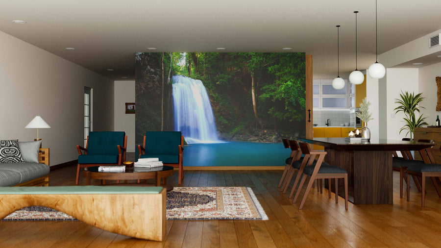 A modern living-dining room features wood floors, teal chairs, a long dining table, and the Erawan Waterfall Wall Mural, bringing tranquility and nature to the space. Warm lighting and rugs add coziness to this contemporary setting.