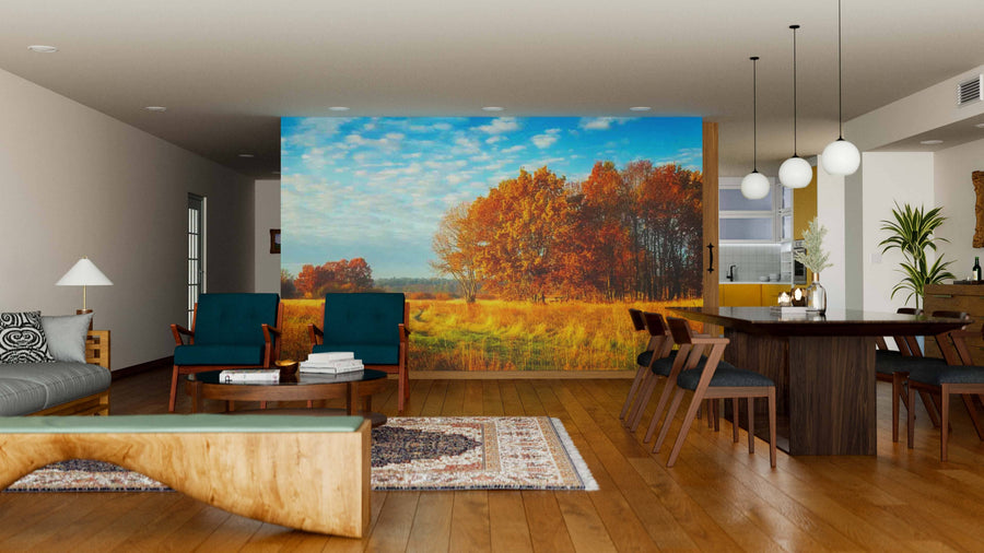 A modern living-dining space with wood floors, teal chairs, a rustic bench, and a rug features the Forest Fall Colors Meadow Wall Mural, bringing vibrant golden trees and blue sky for a cozy autumn-inspired atmosphere.