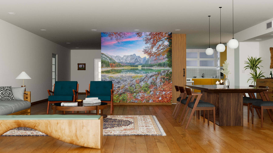 A modern open living-dining area with wood floors, blue armchairs, and a wooden dining table features the Fusine Lake with Mangart Peak Wall Mural. The kitchen has white cabinets, yellow accents, and pendant lights above the table.