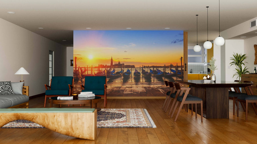 A modern living and dining room with wooden floors and stylish furniture features the Gondolas Wall Mural, a peel and stick artwork of Venetian gondolas at sunset, bringing warmth and vibrant color to the elegant, open space.