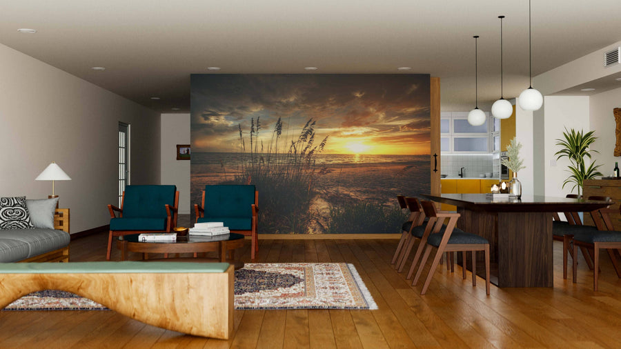 A modern living and dining room with wood flooring, mid-century furniture, globe pendant lights, and a Grassy Beach Sunset Wall Mural featuring clouds, tall grasses, and golden light reflecting on the water.