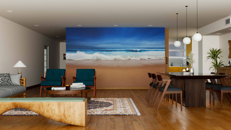 A modern living and dining room with wooden floors, teal chairs, a wood coffee table, and a partial wall showcasing the Heavenly Beach Wall Mural of crashing waves. The dining area features a dark table, six chairs, and three globe pendant lights.