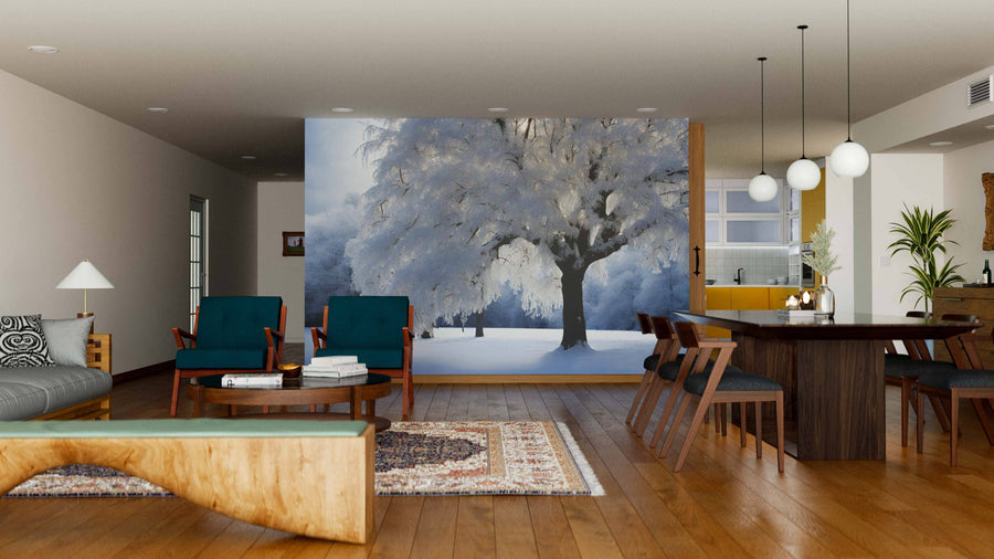 A modern living-dining room boasts wooden floors, dark wood furniture, teal chairs, a patterned rug, and a Heavy Snow-Covered Tree Wall Mural with soft lighting and minimalistic decor. The kitchen is visible in the background.