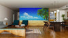 A modern living and dining room features wooden floors, sleek furniture, and the Idyllic Tropical Beach Wall Mural—a peel-and-stick design showing sand, palm trees, and blue sky for a realistic ocean view effect.