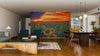 Modern open-concept living and dining area features wood floors, green and wood furniture, and an Illuminated Sunflower Field Wall Mural peel-and-stick at sunset. Pendant lights hang above the table; kitchen is visible in the background.