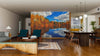 A modern living-dining room with wooden floors and mid-century furniture features the Lake Blue Skies and Fall Colors Wall Mural, creating the illusion of a scenic lake with autumn trees and blue sky indoors.