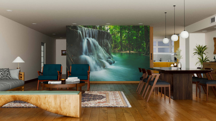 A bright, open living and dining area with wooden floors, teal and brown furniture, a patterned rug, and the Lime Stone Waterfall Wall Mural showcasing a lush green forest. Pendant lights illuminate the dining table.