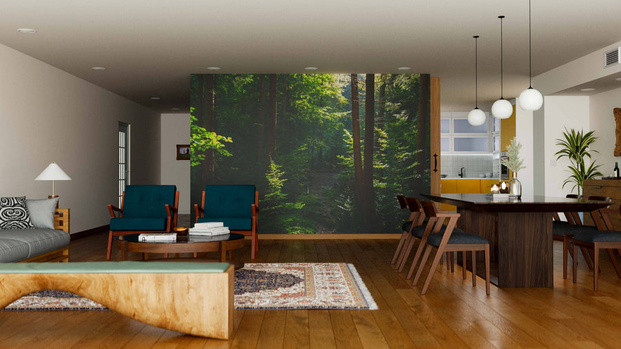 Modern living and dining area with wooden floors, blue chairs, and a large Magical Carpathian Forest Wall Mural. A wooden table with dark chairs sits under globe pendant lights, with contemporary decor and the kitchen visible in the background.