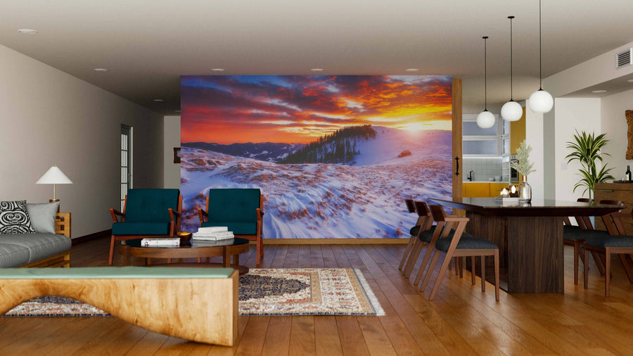 A modern living-dining area with wooden floors and mid-century furniture features the Majestic Winter Trees Glowing Wall Mural depicting snowy mountains at sunset. Spherical lights above the dining table add warmth to this stylish space.