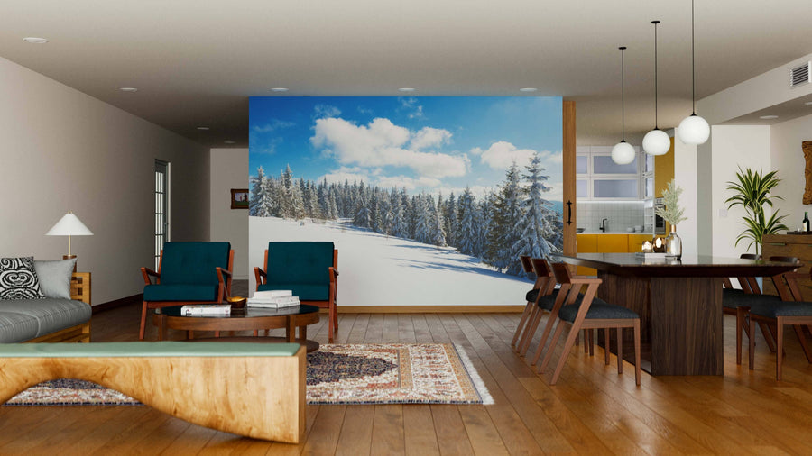 A modern open-plan living and dining area with wooden floors, teal and wood chairs, and a sofa is brightened by the Mesmerizing Picturesque Landscape Wall Mural, depicting a snowy pine forest under a blue sky.