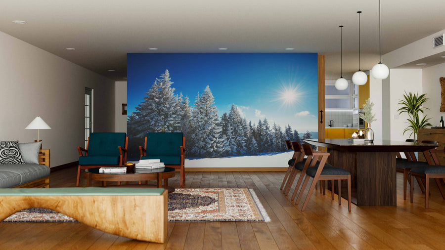 A modern living and dining room features wood furniture, blue-green accents, a patterned rug, and the Mesmerizing Winter Landscape Wall Mural, bringing a snowy forest scene indoors for a cozy wintery ambiance.
