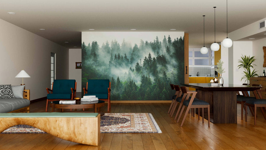 Modern living-dining space with wooden floors, a gray sofa, teal armchairs, the Misty Foggy Forest Wall Mural, a long dark dining table with chairs, spherical pendant lights, plants, and a visible kitchen in the background.