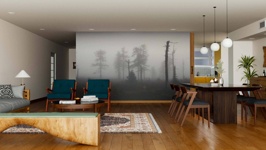 A modern living and dining area with wooden floors features green armchairs, a gray sofa, a wooden bench, and is accented by the Mystical Silhouettes of Trees Wall Mural. The dining space has a dark wood table, chairs, globe pendant lights, and plants.