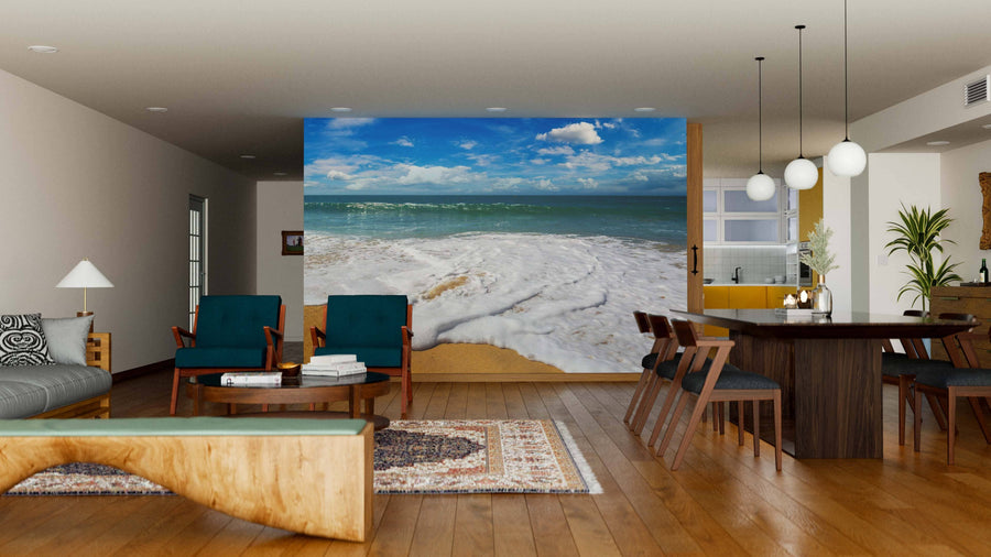 A modern living-dining room with wood floors and mid-century furniture is brightened by the Nazare Coast in Portugal Wall Mural, featuring ocean waves and blue sky. Pendant lights illuminate the rectangular dining table, enhancing the cozy space.
