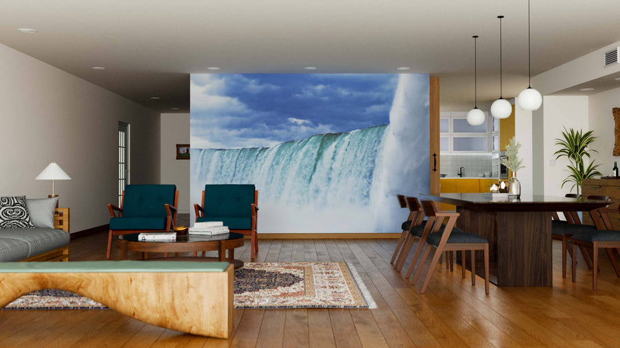 A modern living and dining room with wood floors and mid-century furniture features the Niagara Falls Up Close Wall Mural. The space includes teal chairs, a patterned rug, mixed tables, and globe pendant lights above the dining area.