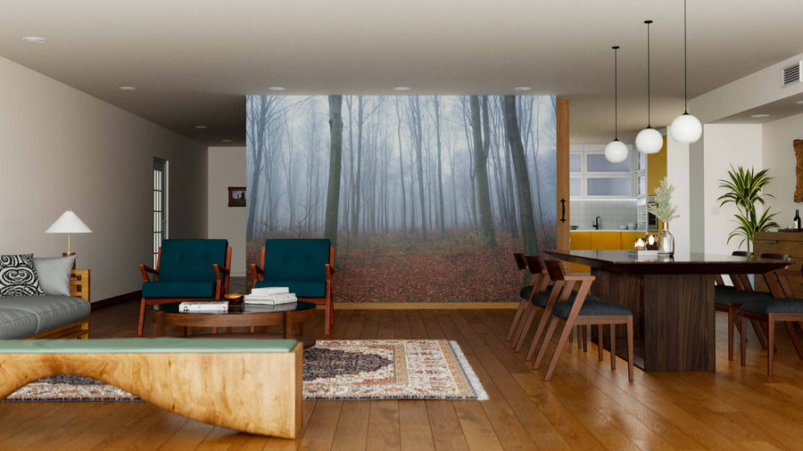 A modern living and dining area with wooden floors, blue chairs, a distinctive coffee table, and hanging lights is highlighted by the November Morning Misty Forest Wall Mural, which brings style and personality to the space.