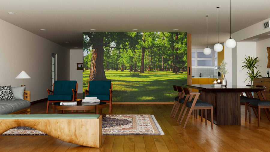 A modern living-dining room with wood floors and mid-century furniture features a Pine Forest with Green Grass Wall Mural. Pendant lights hang over a dark wood dining table; green armchairs and sofa complete the seating area, with a kitchen in the background.