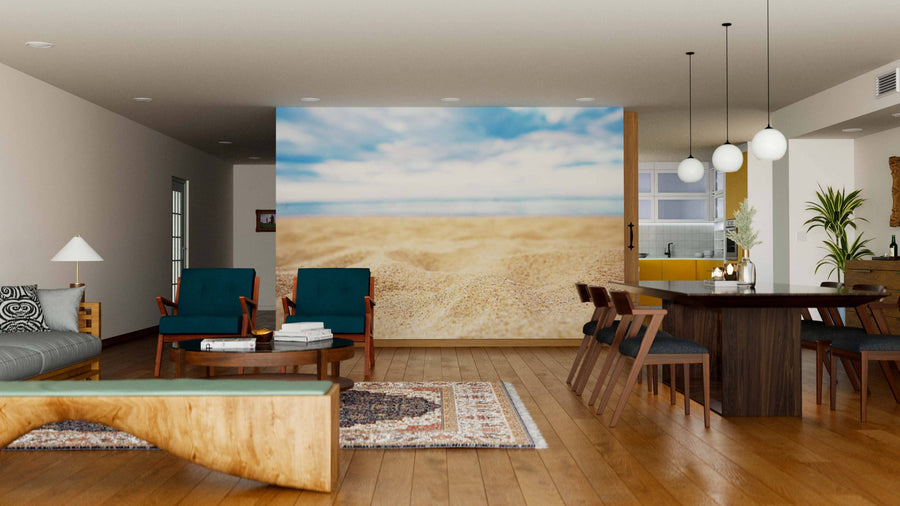 A modern open-plan living and dining area featuring wood floors, mid-century furniture, blue armchairs, a wooden dining table set, pendant lights, an area rug, and the Sand Wall Mural depicting a sandy beach and blue sky.