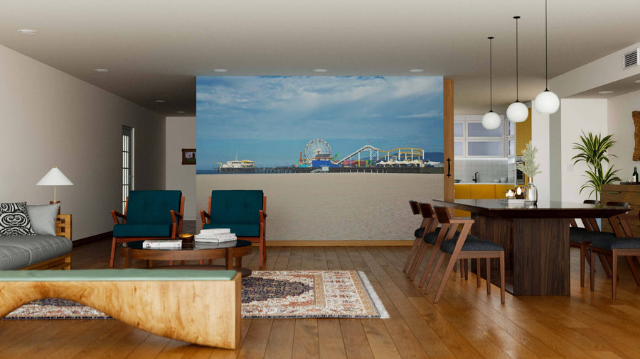 A modern living-dining room with wood floors and stylish décor features the Santa Monica Beach Wall Mural, depicting a seaside amusement park and Ferris wheel under a blue sky, adding an inviting and contemporary touch.