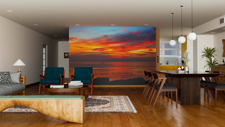 A modern living-dining room features teal chairs, a wooden table, and a unique coffee table. The Seascape Phu Quoc Wall Mural adds warmth with its vivid sunset waterscape. Hardwood floors and rugs complete the look.
