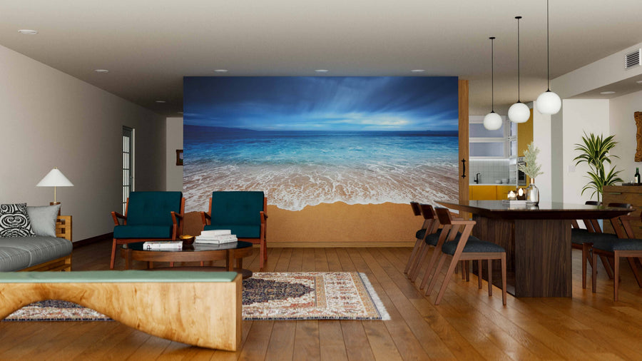 A modern living and dining room features wood floors, contemporary furniture, pendant lights, and the Seaside Storm Wall Mural, creating a serene coastal vibe with an ocean shoreline under a cloudy sky.