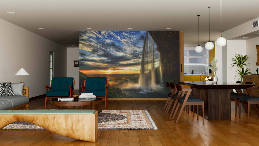 A modern living and dining room features wooden floors, contemporary furniture, and a Seljalandsfoss Waterfall at Sunset Wall Mural. Pendant lights hang above the dining table, with a stylish kitchen visible in the background.