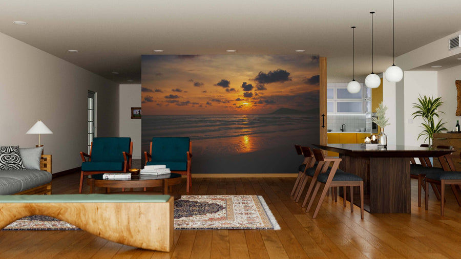 A modern living and dining room features wood floors, mid-century furniture, and the Silhouette of Sea Wall Mural—a dramatic peel and stick mural of a beach sunset with orange clouds reflecting on the ocean, creating a serene focal point.